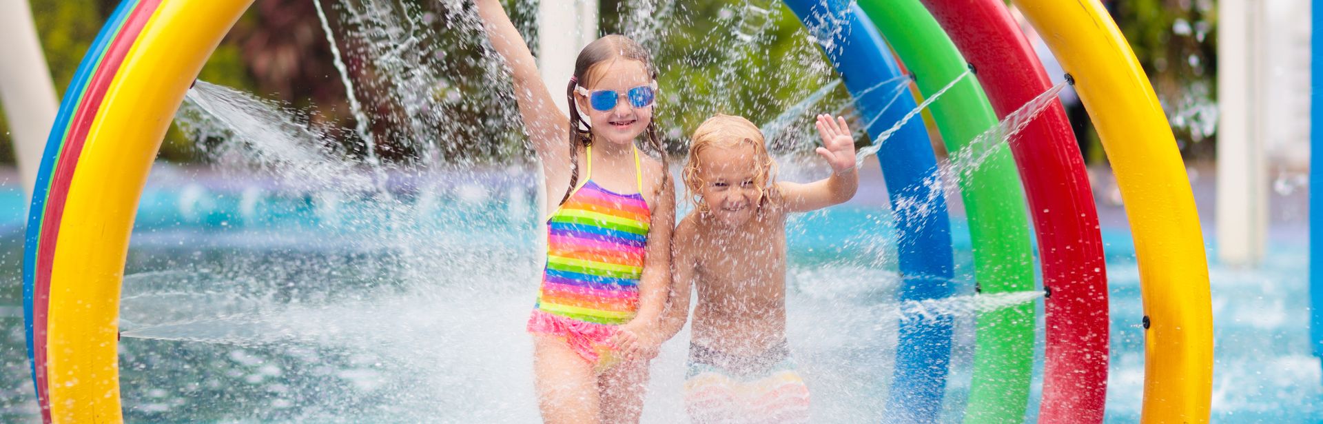 Zwei Kinder laufen durch bunte Bögen aus denen Wasser auf sie gespritzt wird