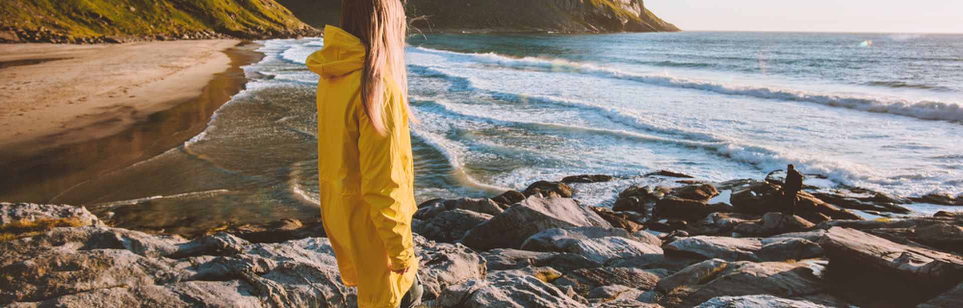 Eine Frau in einer gelben Regenjacke schaut auf das Meer
