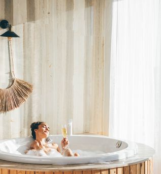 Eine Frau sitzt in einem Whirlpool in einem modernen Hotelzimmer und trinkt ein Glas Sekt
