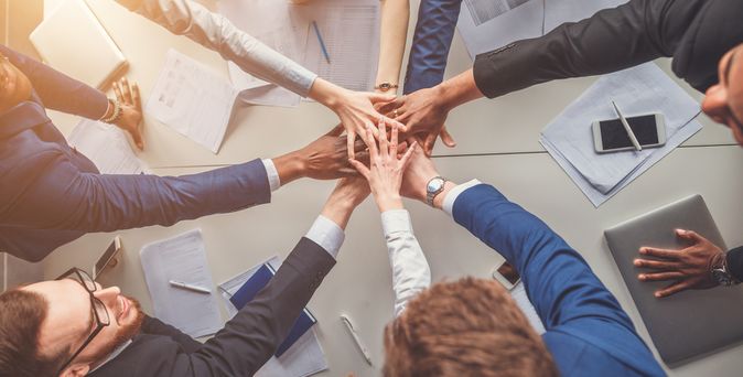 Das Bild zeigt eine Gruppe von Menschen, die jeweils eine Hand in die Mitte strecken