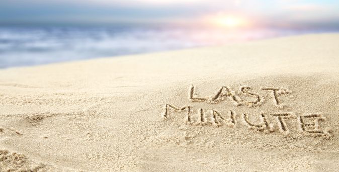 Ein Sonnenuntergang am Strand, im Sand steht "Last Minute" geschrieben