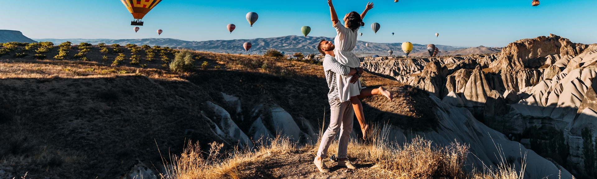 Ein Mann trägt eine Frau im Arm, um Sie herum schweben Heißluftballons durch die Luft