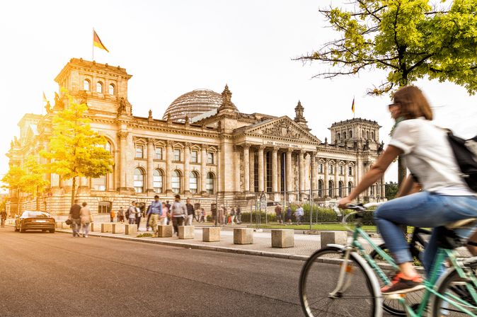 Eine Frau fährt bei Sonnenschein auf dem Fahrrad am Berliner Bundestag vorbei