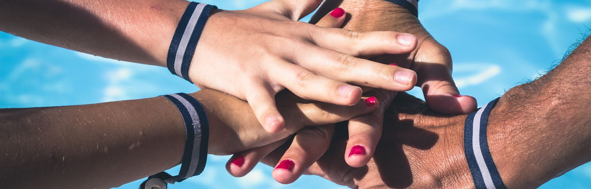 Vier Hände mit Armbändern aufeinander über einem Pool