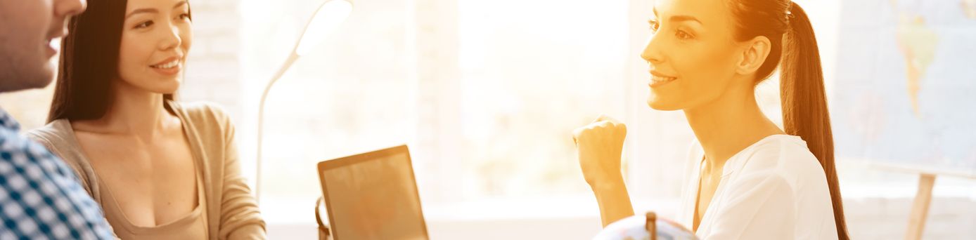Ein Paar sitzt mit einer Reiseberaterin am Tisch, während das Licht durch das Fenster im Hintergrund den Raum erleuchtet