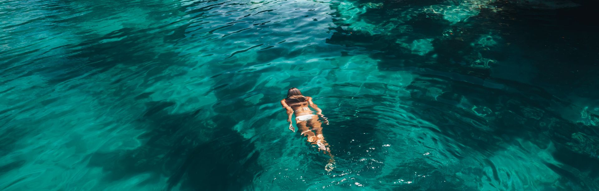 Frau schwimmt im Meer umgeben von Felsen