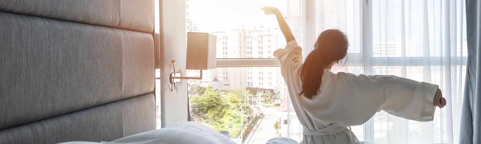 Eine Frau sitzt im Bademantel auf Ihrem Bett und streckt sich 