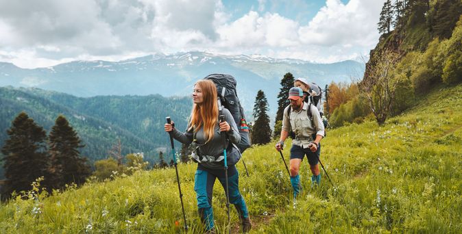 Zwei Personen wandern mit Nordic Walking Stöckern durch eine Wiese