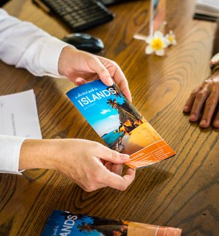 Ein Schreibtisch in einem Reisebüro, der Reiseberater überreicht eine Broschüre zu einem Urlaubsland