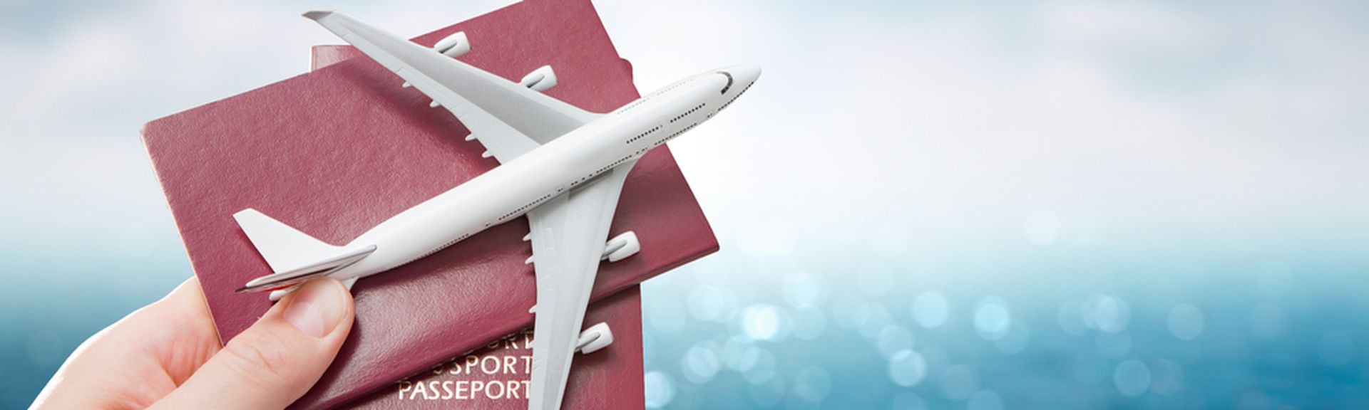 Eine Hand hält vor einem blauen Hintergrund zwei Reisepässe und ein Miniaturflugzeug hoch