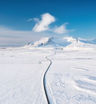 Weg durch eine flache Schneelandschaft mit Bergen im Hintergrund