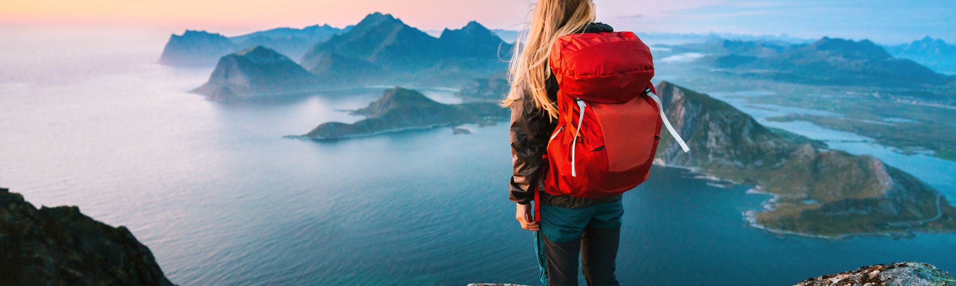 Alleinreisende Frau mit Rucksack schaut von einem Berg auf Wasser 