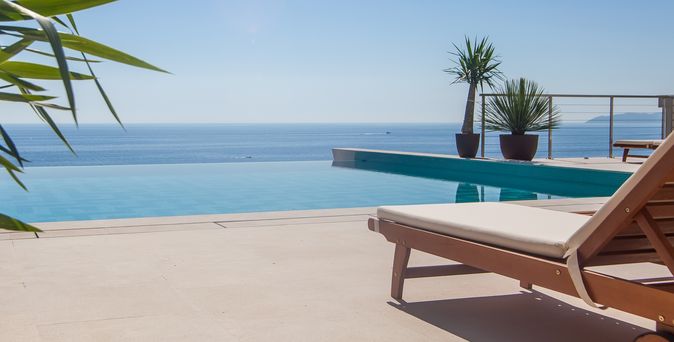 Eine Liege und an einem Infinity Pool, im Hintergrund das Meer