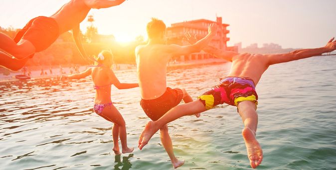 Vier Personen springen bei Sonnenuntergang ins Meer