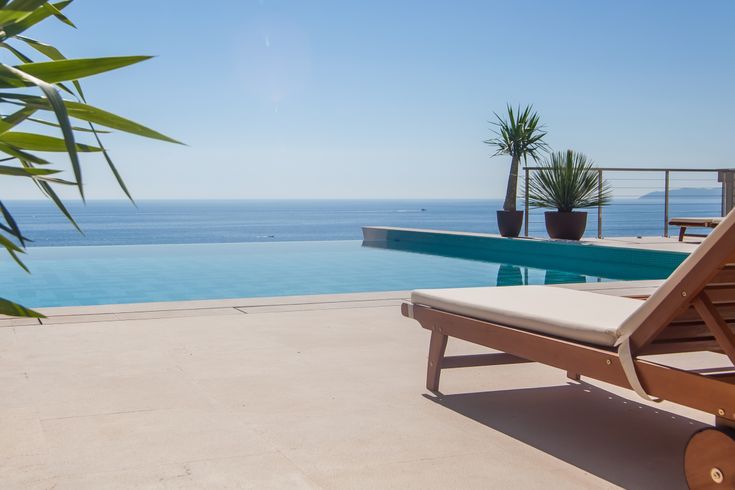 Eine Liege und an einem Infinity Pool, im Hintergrund das Meer