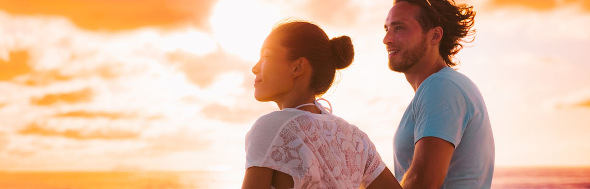 Eine Frau und ein Mann stehen bei Sonnenuntergang an der Reling eines Kreuzfahrtschiffes