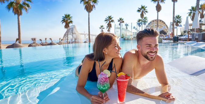 Lachendes Paar trinkt Cocktails, während sie im Pool liegen