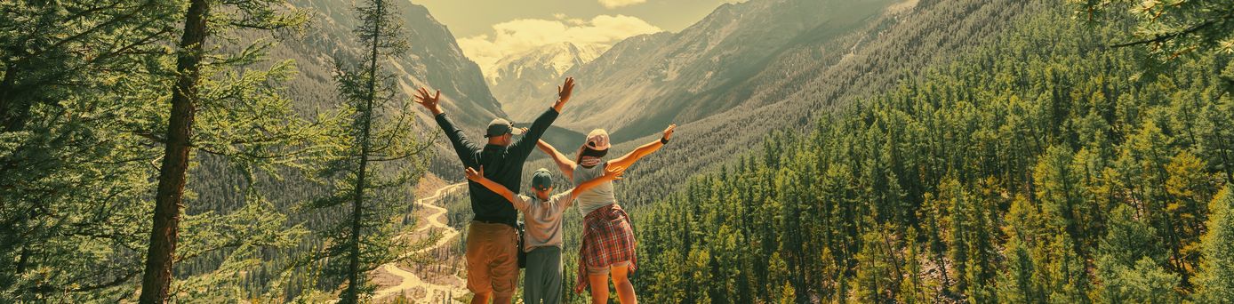 Eltern und Kind schauen beim Wandern gemeinsam auf eine Berglandschaft 