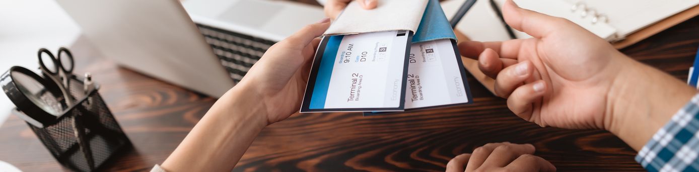 Eine Frau sitzt am Schreibtisch und übergibt zwei Personen Ihre Flugtickets