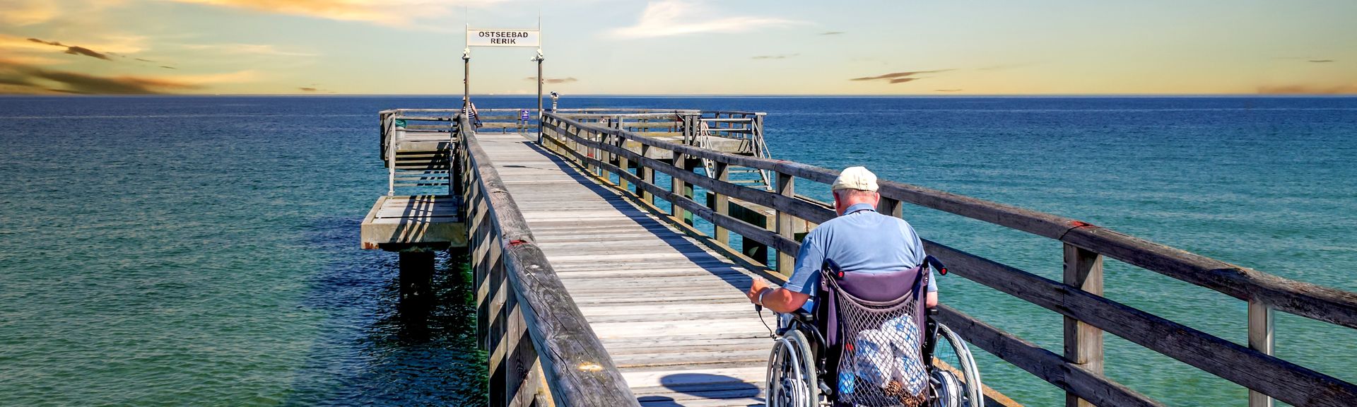 Mann im Rollstuhl auf einer Seebrücke am Meer