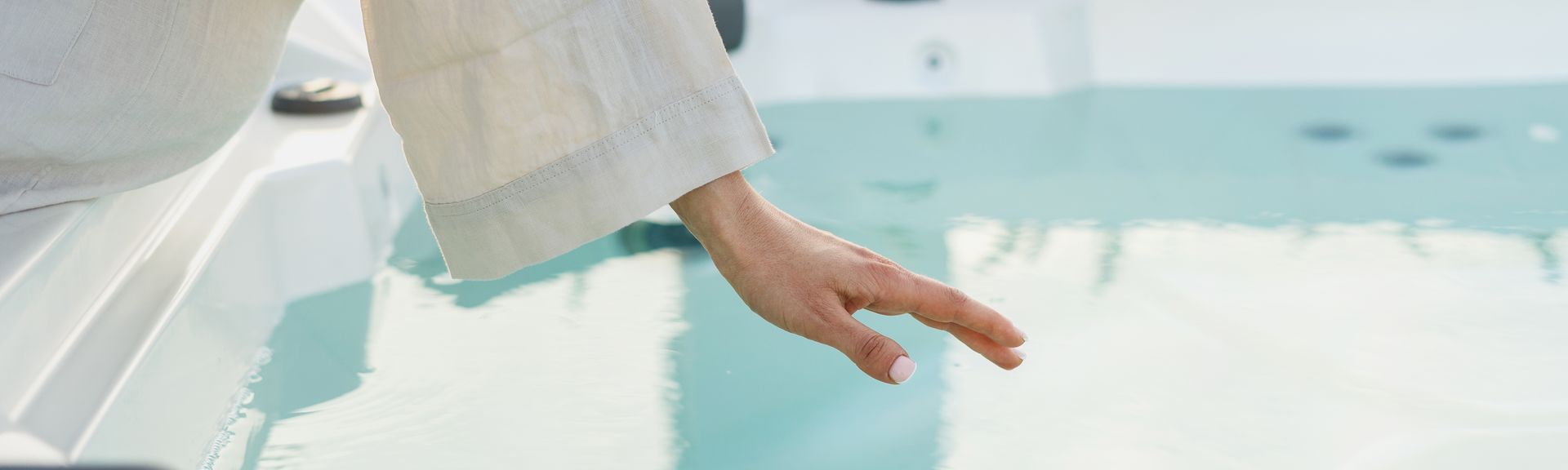 Eine Frau sitzt im Bademantel am Rand eines Whirlpools und hält Ihre Hand über die Wasseroberfläche