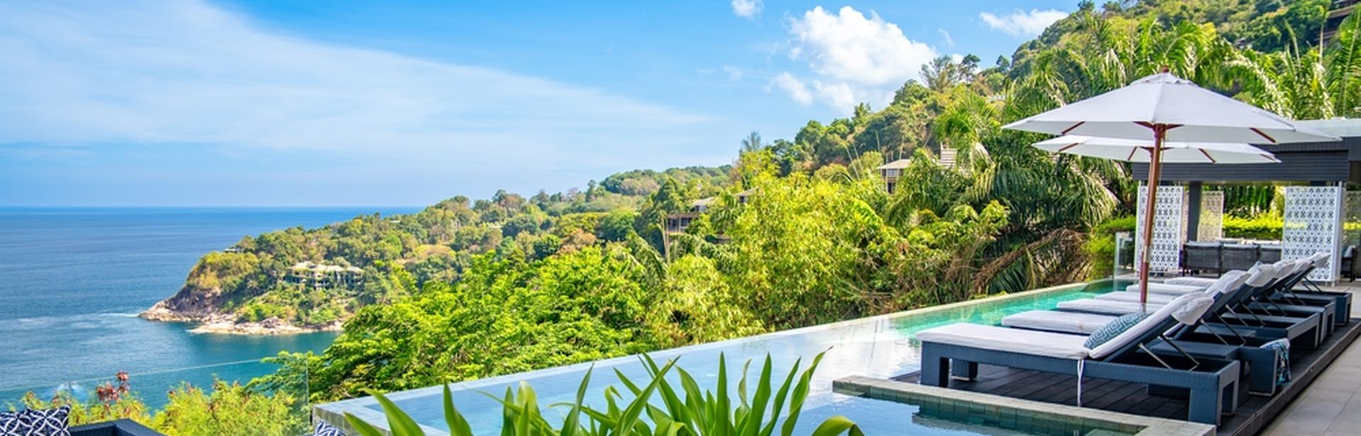Ein eleganter Infinity Pool umgeben von Ledersofas, Liegen und Pflanzen mit Blick auf das Meer