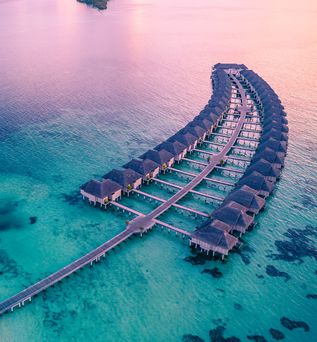 Wasserbungalows vor einem sich wegen einem Sonnenuntergang lila färbendes Meer