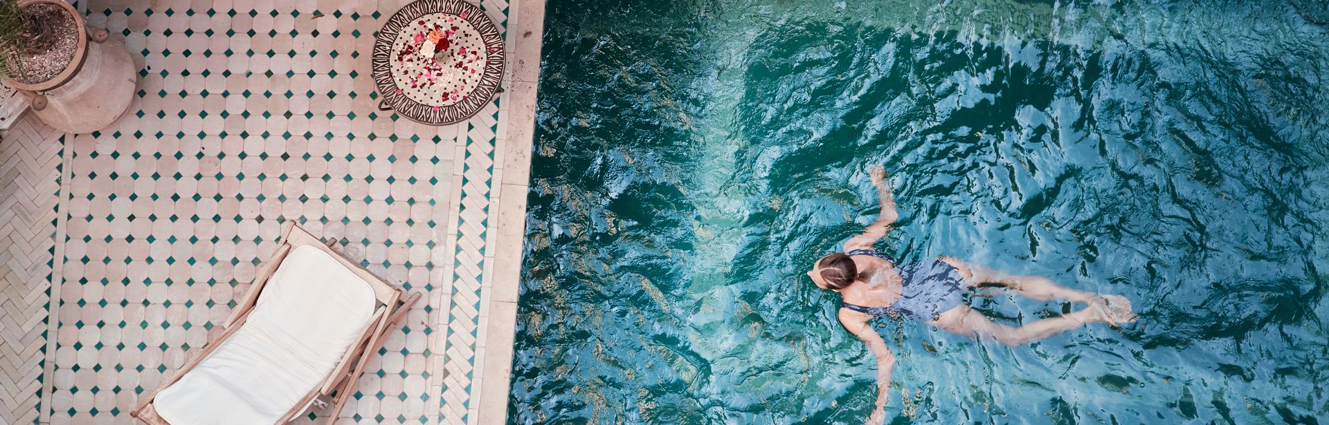 Frau schwimmt in einem Pool; Neben dem Pool, auf der Terrasse steht eine Liege