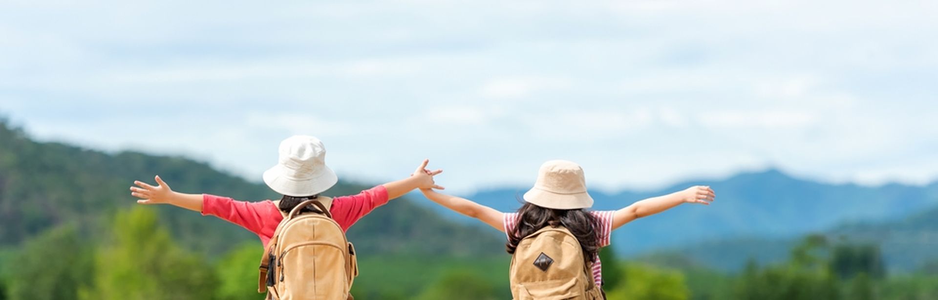 Zwei Mädchen mit Rucksäcken laufen fröhlich einen Weg entlang und heben die Arme in die Luft