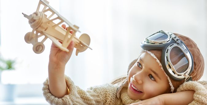 Junge trägt einen Fliegerhelm und spielt mit einem Modellflugzeug