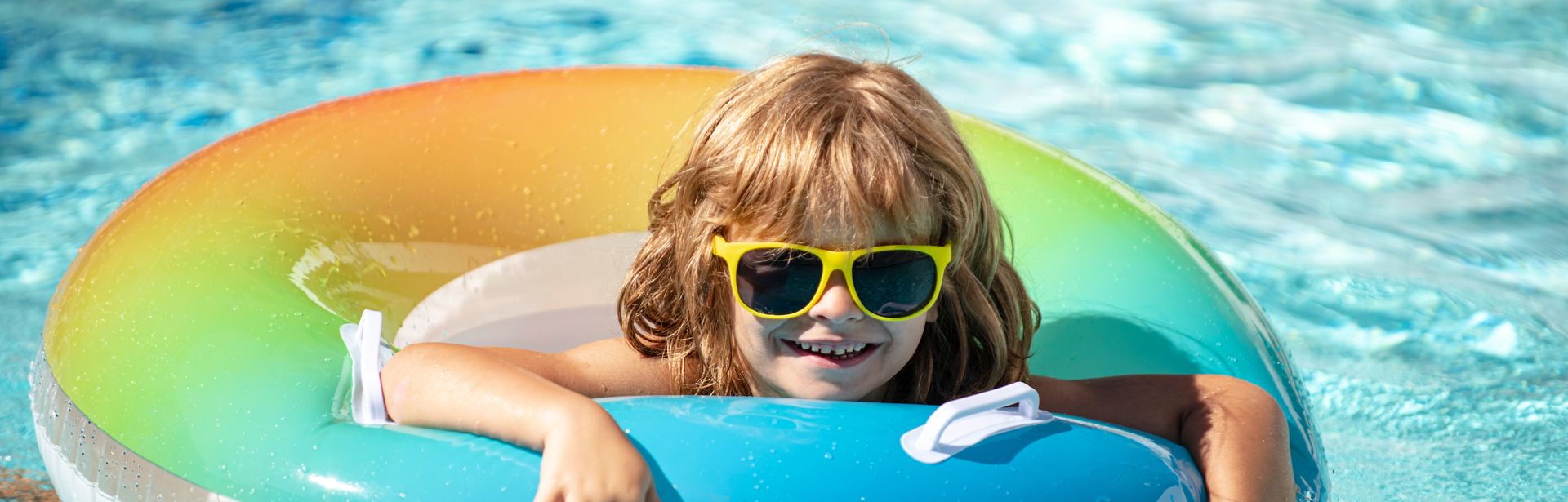 Ein Kind mit einer Sonnenbrille in einem bunten Poolring