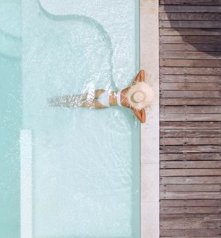 Eine Frau mit weißem Sonnenhut lehnt am Rand eines eleganten Pools