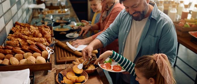 Eine Familie bedient sich lachend an einem Frühstücksbuffet