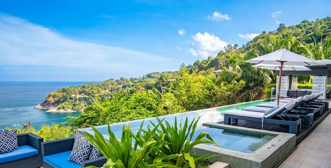 Ein eleganter Infinity Pool umgeben von Ledersofas, Liegen und Pflanzen mit Blick auf das Meer