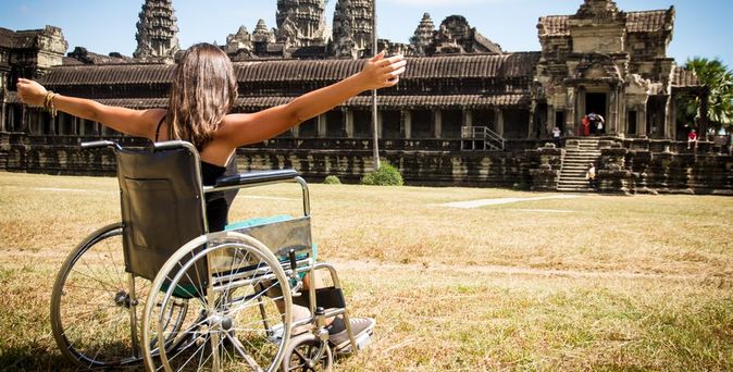 Frau im Rollstuhl vor einem Tempel und hebt die Arme