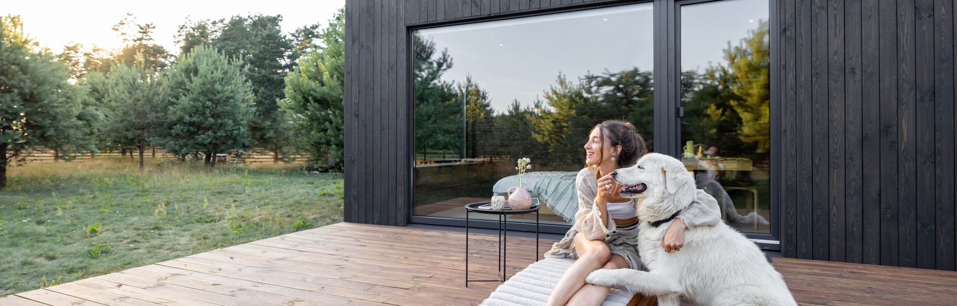 Eine Frau sitzt mit Ihrem Hund auf der Terrasse von einem Ferienhaus