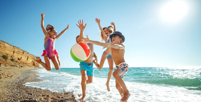 Eine Gruppe von Kindern spielt mit einem Ball am Strand und springen alle in die Luft
