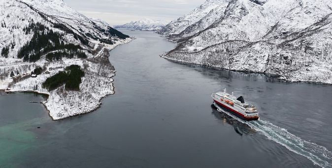 Ein Kreuzfahrtschiff fährt durch einen Fjord, umgeben von schneebedeckten Bergen und winterlicher Landschaft.