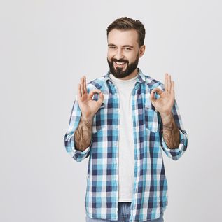 Mann steht vor weißem Hintergrund, lächelt in die Kamera und zeigt das OK Zeichen mit beiden Händen