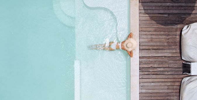 Eine Frau mit weißem Sonnenhut lehnt am Rand eines eleganten Pools