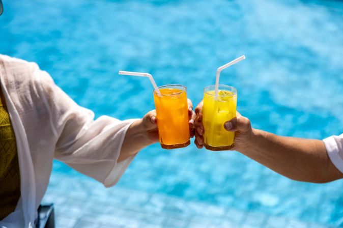 Zwei Hände stoßen mit Gläsern über einem Pool an