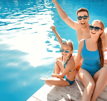 Eine Familie sitzt auf einem Steg und hält lächelnd die Arme in die Luft
