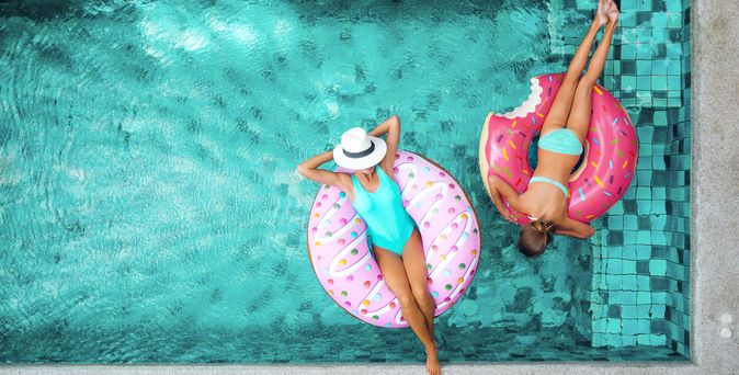 Zwei Frauen liegen in Donut Pool Floaties im Pool