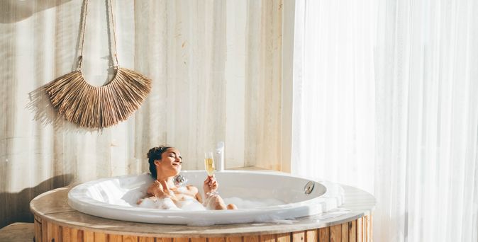 Eine Frau sitzt in einem Whirlpool in einem modernen Hotelzimmer und trinkt ein Glas Sekt