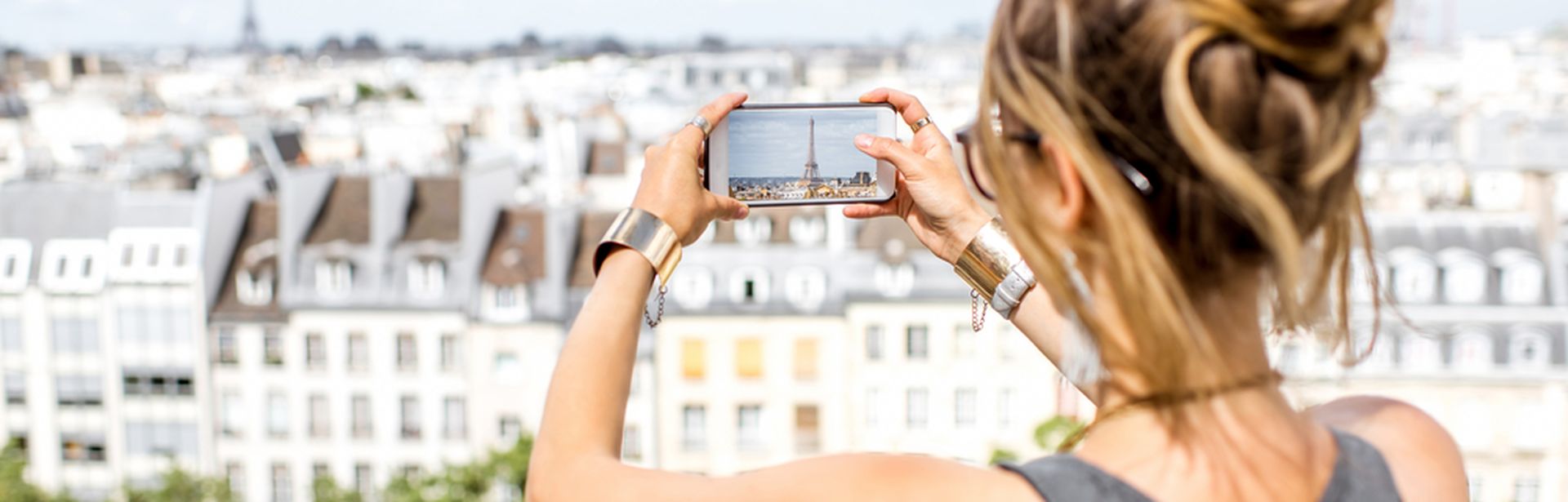 Eine Frau macht mit ihrem Handy ein Foto von einer Stadt, welche sie von einem höher gelegenen Aussichtspunkt betrachtet