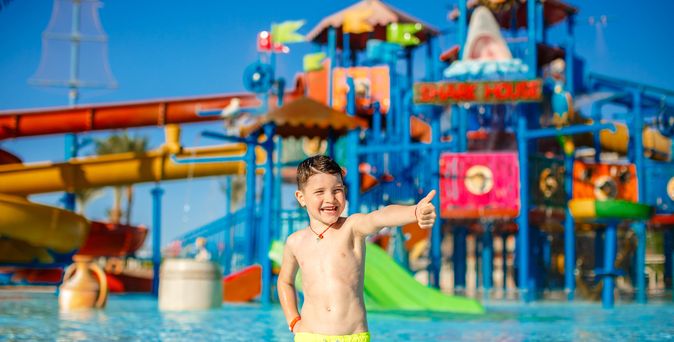 Junge steht vor einem Aquapark und zeigt einen Daumen hoch