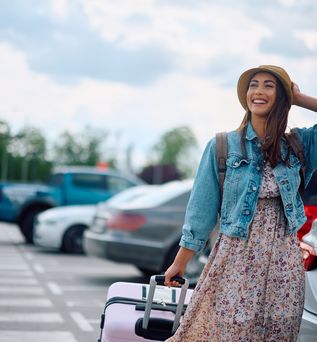 Eine lachende Frau zieht ihren Koffer über einen Parkplatz