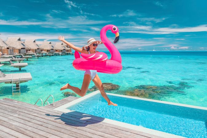 Eine Frau springt lachend mit einem Flamingo Schwimmreifen in einen Pool 
