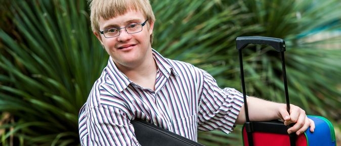 Junger Mann mit einem Koffer und einer Tasche in der Hand umgeben von Pflanzen