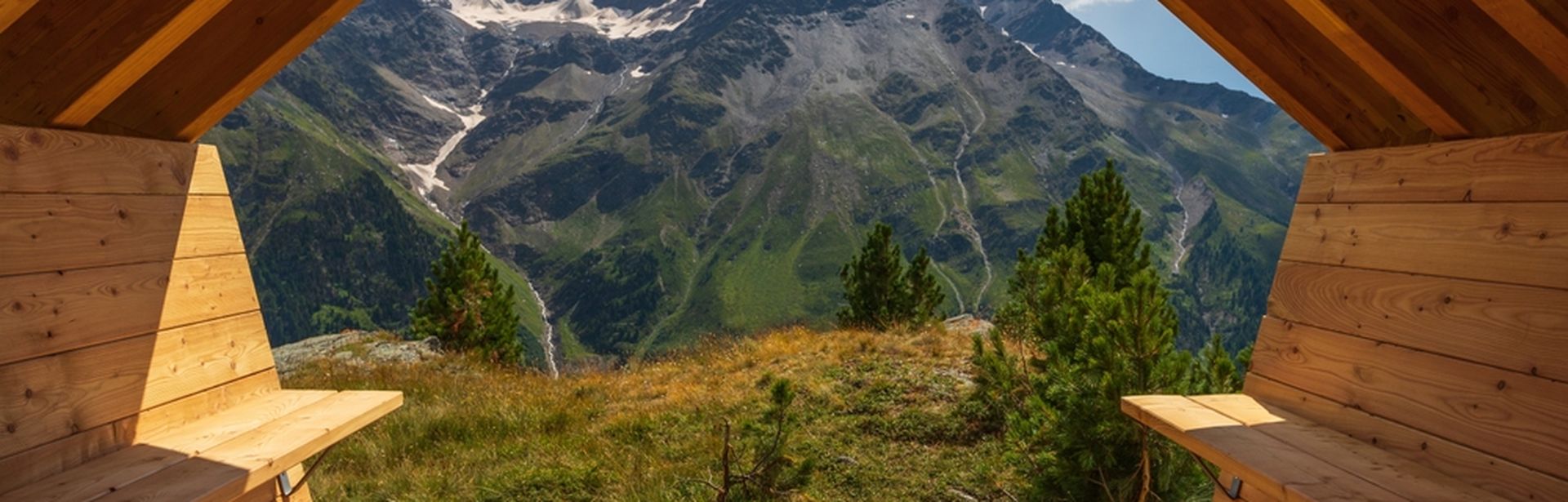 Aus einer Holzhütte mit zwei Bänken schaut man auf eine beeindruckende Berglandschaft